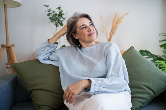 Hopeful woman with grey hair relaxing on sofa in bright living room