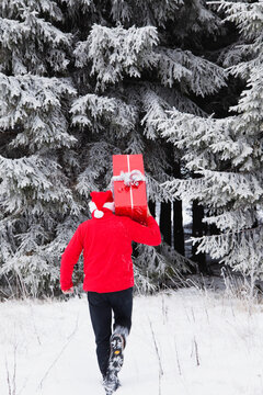 Person in Santa hat carrying Christmas gift in snowy High Venn forest