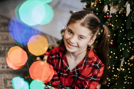 Smiling child in plaid shirt by decorated Christmas tree indoors