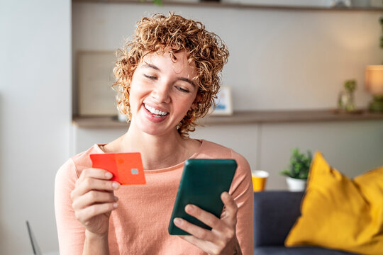 Curly-haired woman smiling and shopping online with smartphone and credit card