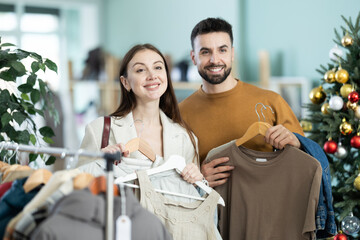 Happy elegance european couple examine and choose new clothes in big modern store, woman selecting dress and man choosing t-shirt