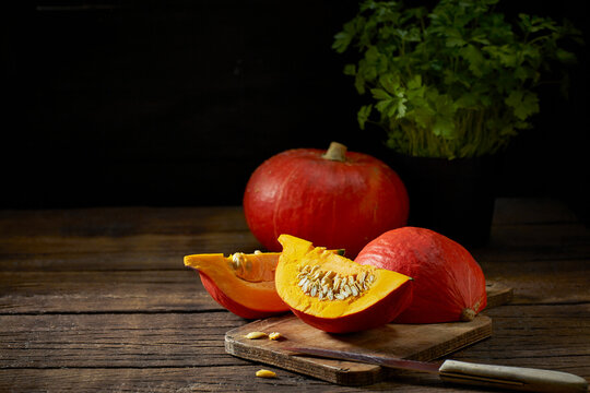 Fresh pumpkin sliced on cutting board with knife and herbs