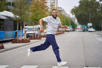 Smiling man running energetically on city street in casual style