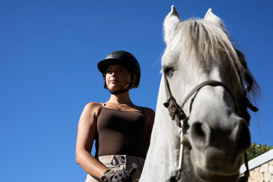 Equestrian wearing helmet riding white horse outdoors on sunny day