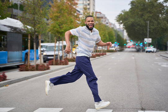 Smiling man running energetically on city street in casual style
