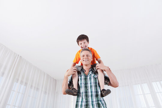 Smiling man giving a shoulder ride to a laughing child indoors
