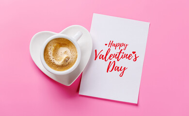 Heart-shaped cappuccino cup and greeting card on pink background