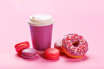 A cheerful display of colorful macarons, donuts, and a paper coffee cup on a pastel pink background