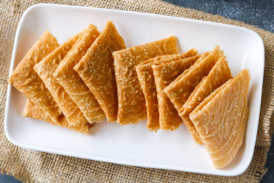 Top view of crispy, golden-brown Kue Semprong or Love Letter cookies, a thin, folded Southeast Asian snack. Arranged on a white plate.