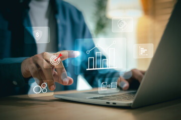 businessman analyzes business growth on a holographic screen, tapping a target icon while working on a laptop. The image depicts data analysis, financial planning, and goal setting for future success.