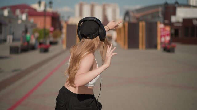 caucasian woman dancing away from camera arms raised in ecstatic motion, acts as festival attendee celebrating beats, leads spontaneous choreography as flashmob leader, embraces freedom as city