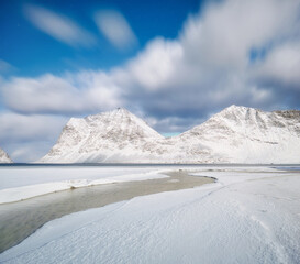 Dramatic night view of Haukland Beach in Lofoten, Norway. Night in the fjord. Winter landscape with snow on the beach, majestic mountains, and long exposure motion blur clouds. Arctic nightscape. 