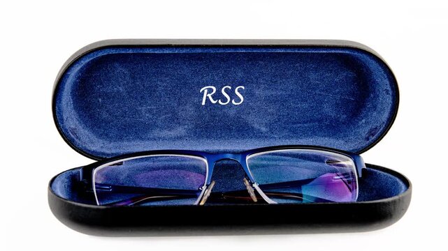 A pair of blue framed spectacles rests inside a dark blue velvet lined case. The initials RSS are stylishly embossed above the glasses in the soft, velvety lining of the case
