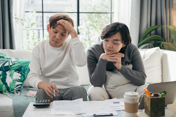 Stressed Asian gay couple sitting at a table, overwhelmed with many bills and financial documents. Two men worrying about debts, economic crisis, and household budget problems in their home office.