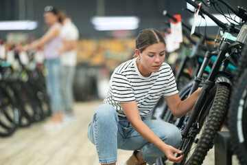 Young buyer female checking tire on wheel in sports bicycle store