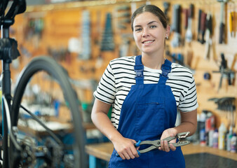Young woman bicycle repair service worker in uniform posing with tool