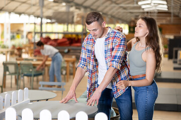 Interested young couple thoughtfully evaluating patio furniture options in garden store, choosing comfortable and functional table for friendly gatherings