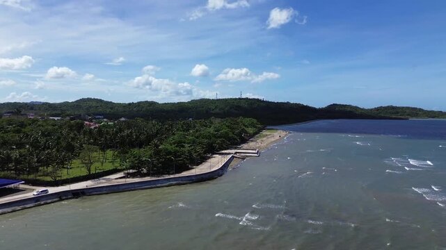 Aerial drone footage of the coastal seawall in Odiongan City on Tablas Island, Philippines, showing a concrete beachfront promenade with palm-lined shoreline, blue sea, and hills in the background.