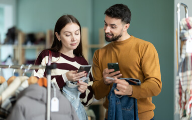 Married couple choosing jeans together in a clothing store, they scan the QR code on the tags for detailed information on the store website. Shoppers pay for items in the app