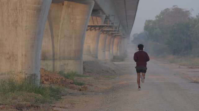 A lone runner jogging outdoors under a concrete bridge, embracing an active lifestyle and personal fitness routine. Urban exercise, endurance training, and healthy living concept with copy space.