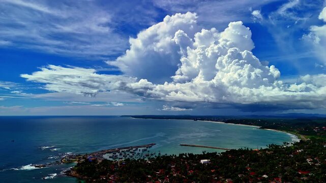 Aerial panorama of Dondra Head coastline in Sri Lanka with dramatic cumulus clouds, turquoise sea, and lush green shoreline stretching into the horizon.