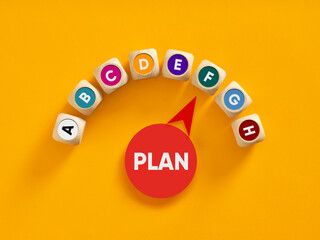 Plan a to h business strategy on colorful wooden blocks and gauge pointing to plan text on yellow background