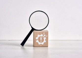 Magnifying glass inspecting wooden cube with alert symbol inside gear