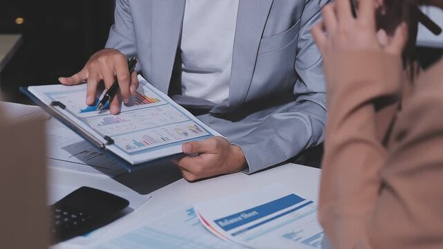 Two women are looking at a table with many papers and graphs. One of the women is holding a pen