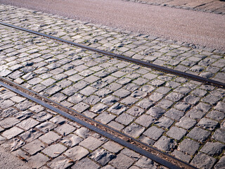 Tram tracks embedded in cobblestone street in historic old town. Urban transport infrastructure, stone pavement, city street detail.