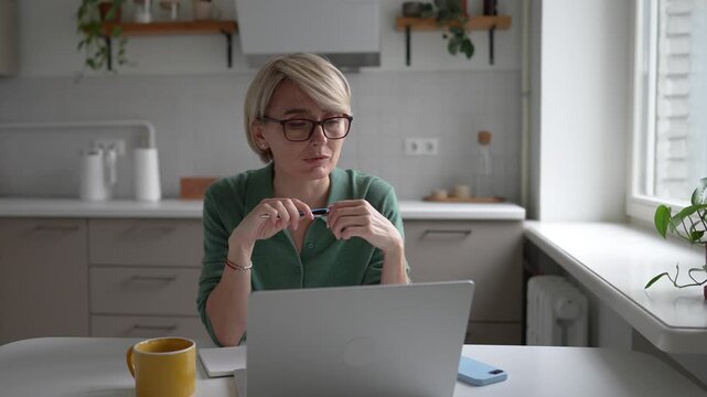 Middle aged business woman with ADHD working on laptop at home, worried and anxious expression, nervously clicking pen in hands, getting distracted by thoughts, has problems with concentration.
