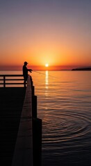 Fototapeta premium Lone individual casts fishing line from wooden pier during vibrant orange sunset over calm water