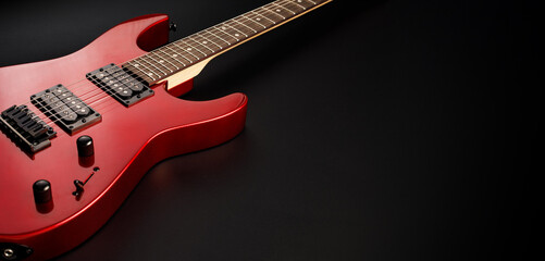 Red electric guitar resting on black background for music