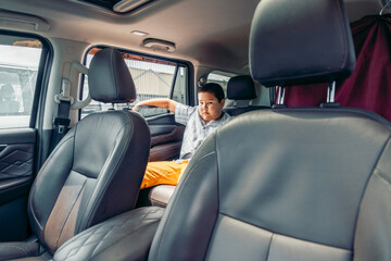 A young Asian boy sits in the back seat of a car, looking out the window. The interior features leather seats and a relaxed atmosphere, suggesting a family trip.