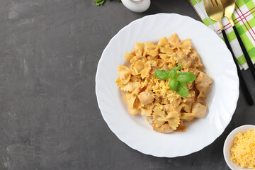 Pasta farfalle with turkey in tomato-sour cream sauce, cheese and basil on white plate, Top view