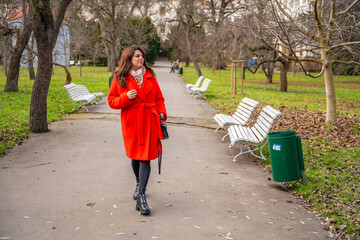 Woman walking in park in Prague during winter without snow wearing red coat. Calm urban walking, everyday lifestyle and seasonal city routine in real life European environment