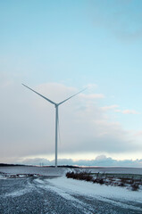 Wind turbines standing in an open rural landscape during a winter snowstorm.