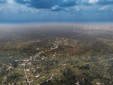 Aerial view of the landscape where the dark clouds meet the horizon, casting shadows over the sparse vegetation and buildings, Obor Road, Egbema, Rivers, Nigeria.