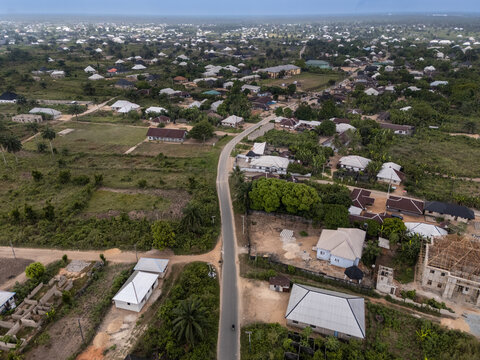 Aerial view of a winding road slicing through green foliage and sparsely dotted buildings under an overcast sky, Egbema, Rivers, Nigeria.