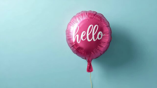 Cheerful pink mylar balloon with the word hello written in a white cursive font floating and slowly moving against a solid pastel blue wall, representing a friendly and positive greeting