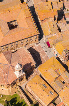 Aerial view of Piazza Pio II bathed in warm sunlight, with the terracotta rooftops creating a textured landscape, Pienza, Tuscany, Italy.