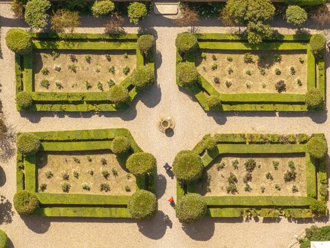 Aerial view of geometrically precise gardens with manicured hedges casting long shadows, contrasting with the earthy tones of the pathways and the central fountain, Pienza, Tuscany, Italy.