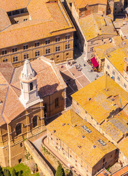 Aerial view of terracotta rooftops and the Piazza Pio II, creating a warm, textured tapestry against the azure sky, Pienza, Tuscany, Italy.