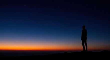 Fototapeta premium Lone figure stands silhouetted against a twilight horizon displaying rich color gradients