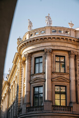Fototapeta premium Monumental Classical Building In Munich: Curved Stone Facade With Sculptural Figures, Arched Windows, And Warm Sunlight In Historic Urban Setting