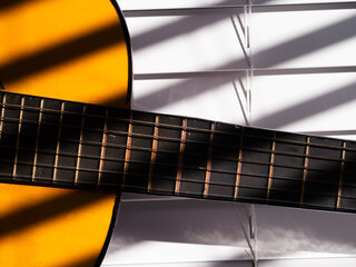 Fototapeta premium Acoustic guitar in sunlight through slat blinds