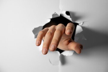 A hand reaching through a torn hole in a white background
