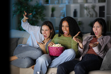 Angry diverse friends watching tv in the night at home