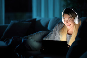Happy woman wearing headphone in the night watching media