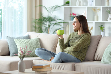 Happy woman in green drinking tea or coffee looking at side