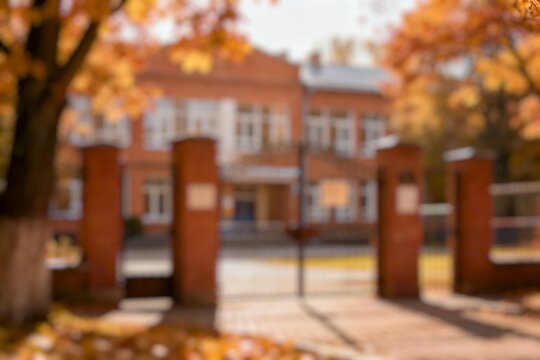 Blur imagebof  school gate with autumn leaves and brick building, warm daylight, calm education background.